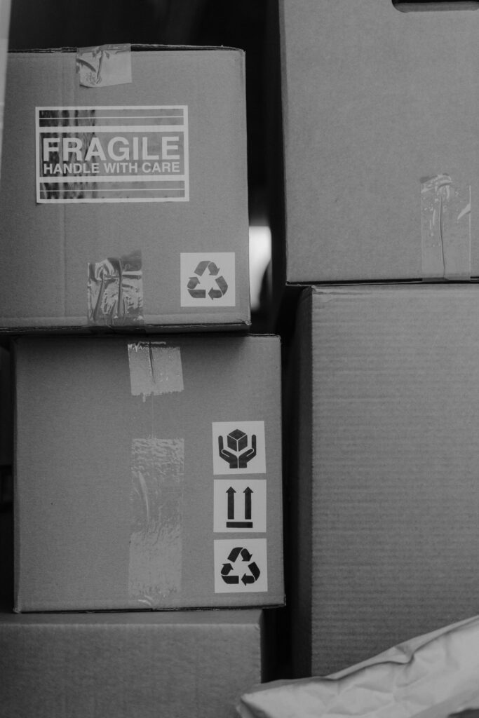 pexels-photo-6170157-6170157 Monochrome image of stacked cardboard boxes with fragile and recycling symbols.